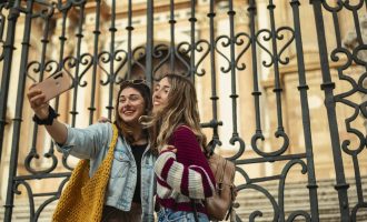 Two happy tourist friends take a selfie in front of the cathedral of Malaga.